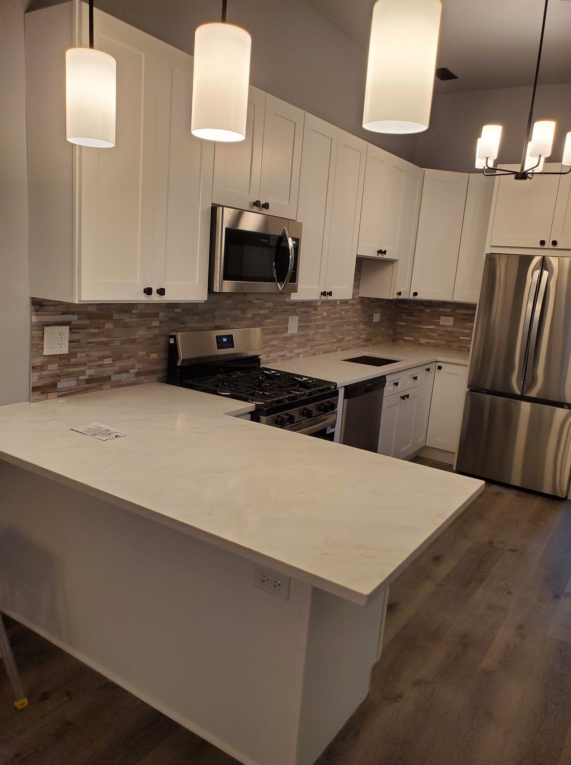 White shaker kitchen remodel with marble countertops and pendant lighting by Too Much Construction
